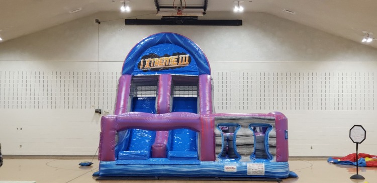 Large inflatable slide and obstacle combo set up inside a gymnasium for indoor event use