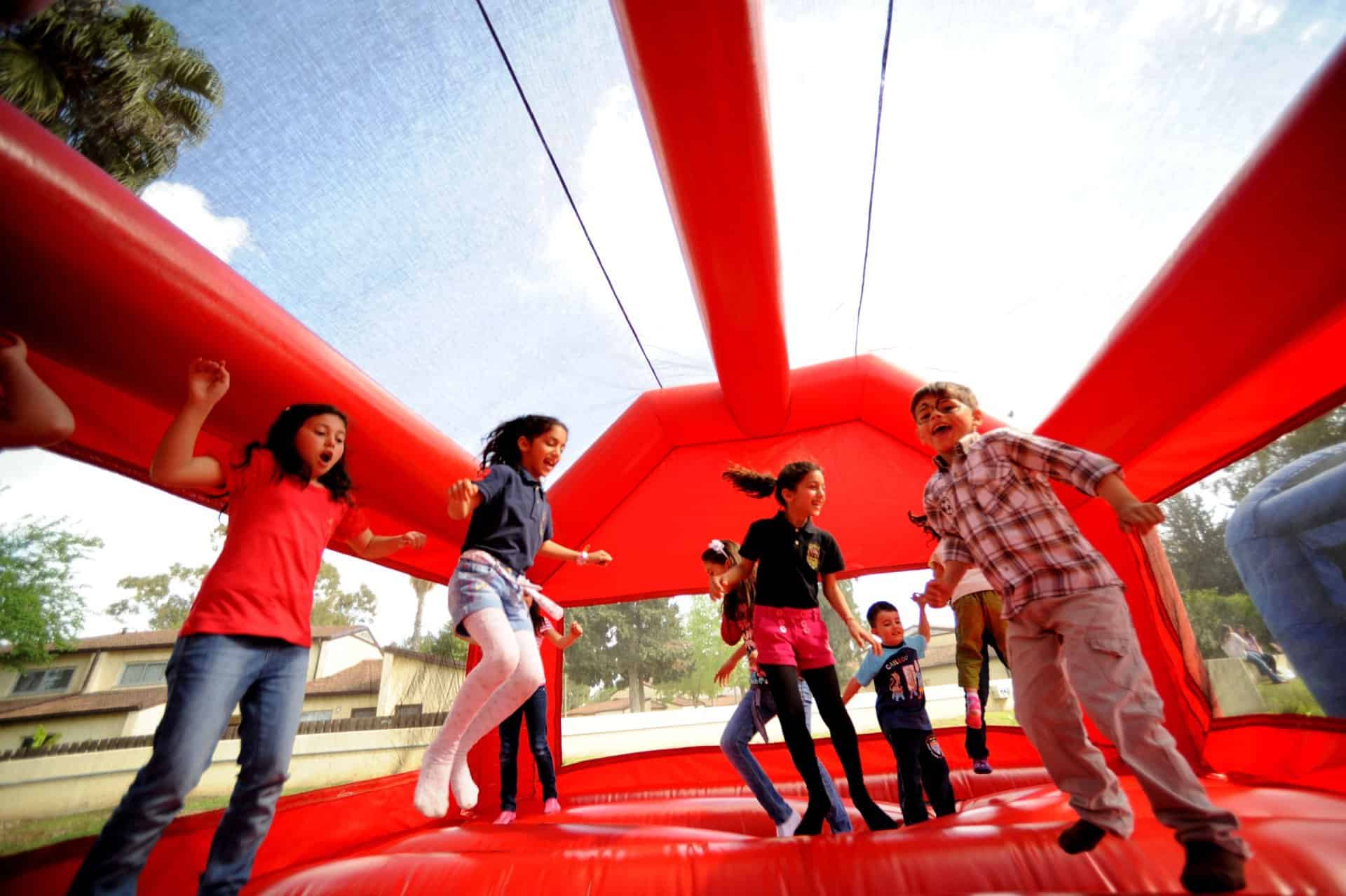 Group of children jumping and playing inside a red inflatable bounce house at an outdoor party event